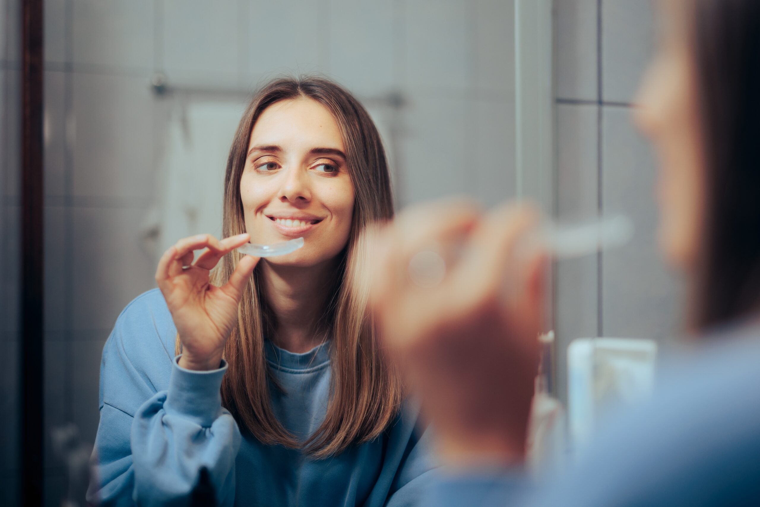 Woman Taking off Her Clear Retainer in the Bathroom Mirror, teeth grinding protection at night